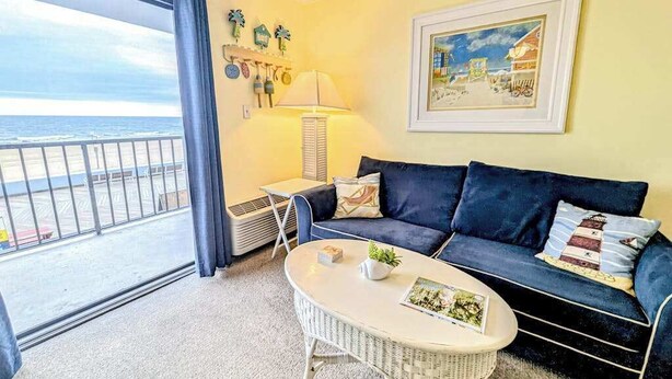 A room with a balcony, a sofa, a small table, a lamp, and a framed picture. - Decatur House 207 (Ocean City)