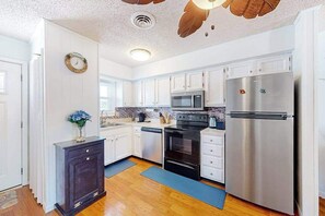 A modern kitchen with white cabinets, stainless steel appliances, and a wooden floor. - Water view condo with peaceful balcony, open layout, smart TVs, games, & W/D (Ocean City)