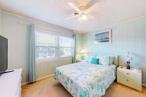 A bedroom with a bed, a nightstand, a lamp, a ceiling fan, and a window with blinds. - Water view condo with peaceful balcony, open layout, smart TVs, games, & W/D (Ocean City)