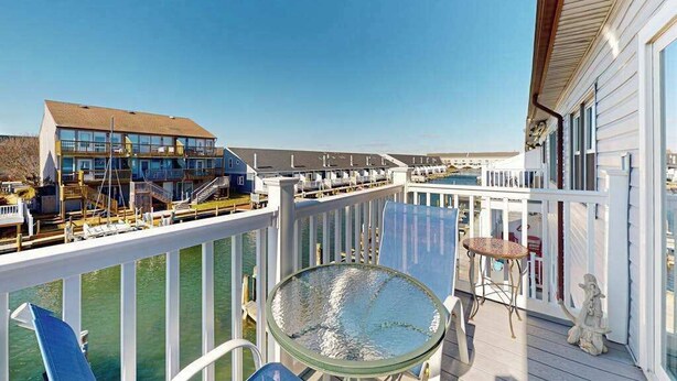Ein Balkon mit Glastisch und Stühlen, einem weißen Geländer und Blick auf ein Gebäude über dem Wasser.