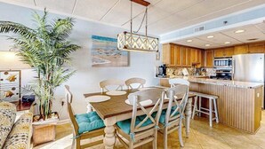 Een eethoek met een houten tafel en stoelen, een hanglamp, en een keuken met houten keukenkastjes en een roestvrijstalen koelkast.