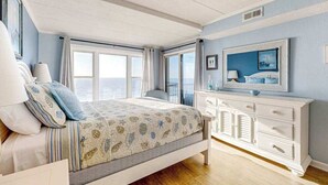 Een slaapkamer met een bed, een dressoir, een televisie en grote ramen.