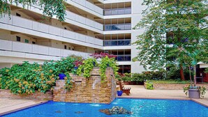 Un hotel con piscina, una cascata in pietra e un giardino ricco di piante.