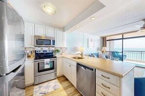 A modern kitchen with stainless steel appliances, a dishwasher, and a view of the ocean. - Fountainhead Towers 1606 (Ocean City)