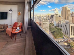 A balcony with a city view, a chair, a table, and a floor lamp. - Vem pro Mirante (São Paulo)