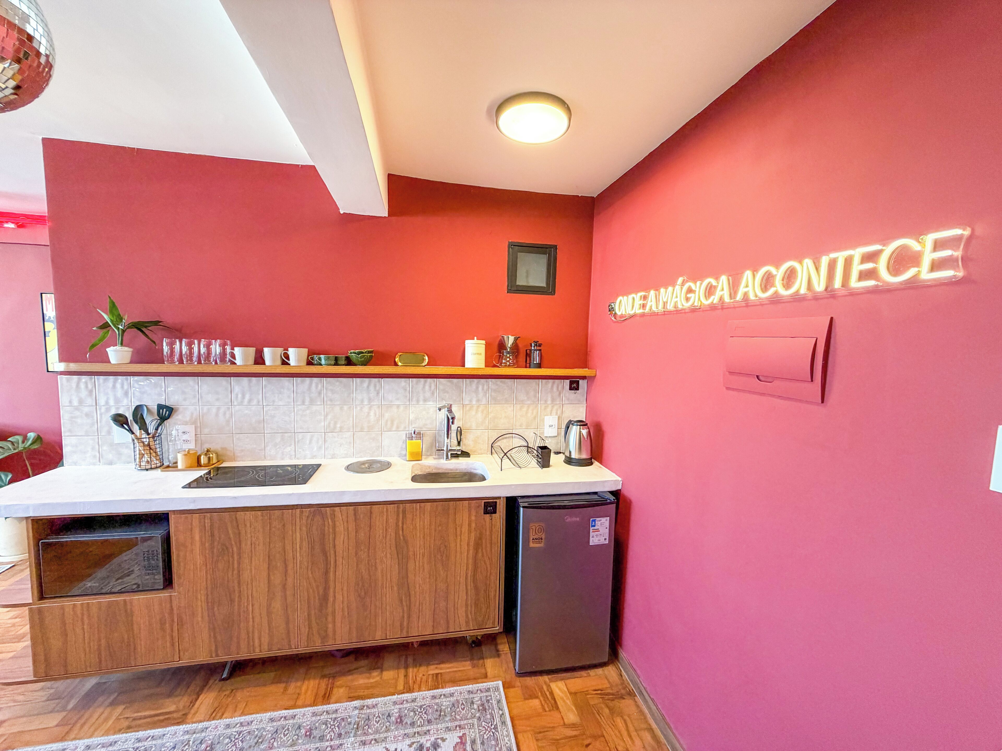 A compact kitchen with a wooden cabinet, a sink, a coffee machine, and a refrigerator.