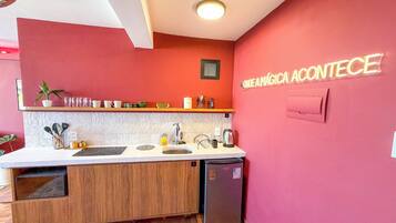 A compact kitchen with a wooden cabinet, a sink, a coffee machine, and a refrigerator.