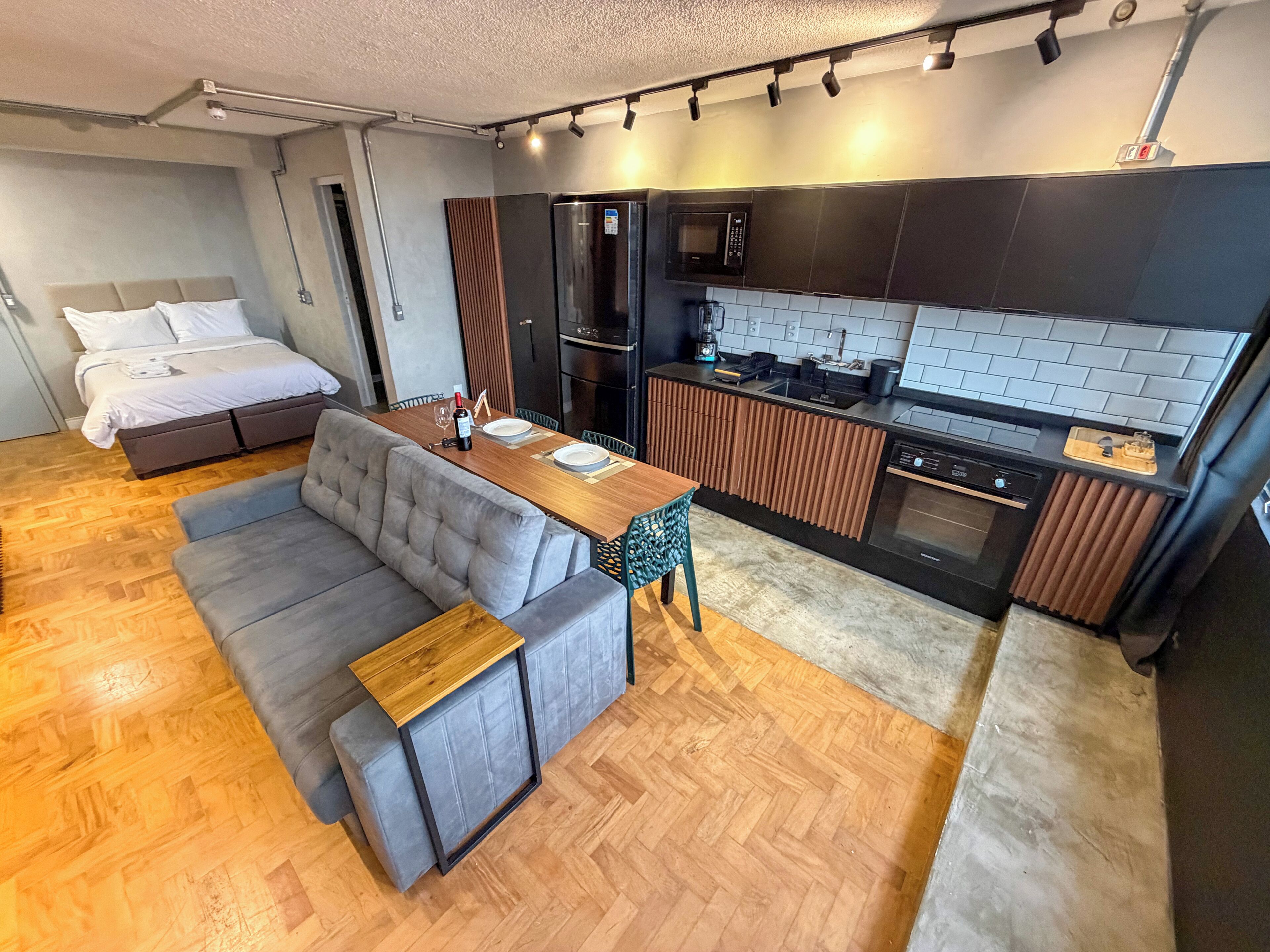 A compact living space with a sofa, a dining table, a kitchenette, and a bed.