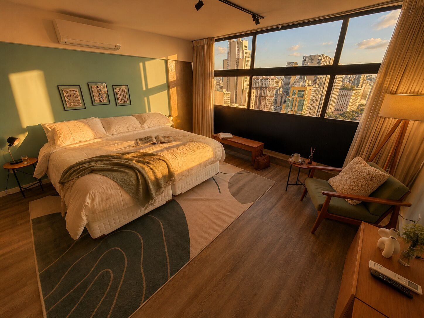 A modern hotel room with a large bed, a seating area, a view of the city, and a window with curtains.