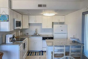A compact kitchen with white cabinets, a microwave, a coffee maker, a dishwasher, and a granite countertop. - Bimini # 207 (Ocean City)