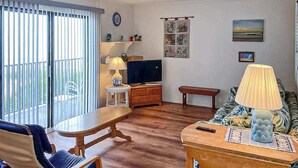 Una sala de estar con televisor, sofá, mesa y una silla.