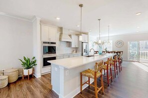 A modern kitchen with white cabinetry, a central island with bar stools, and a large window providing natural light.