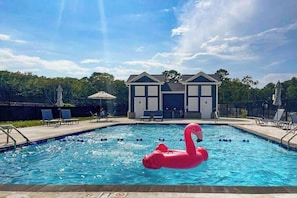 A swimming pool with a pink flamingo float, lounge chairs, and a building with a blue and white facade.
