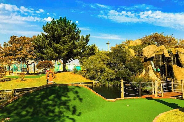 Een minigolfbaan met een vijver, bomen en een kleine brug.