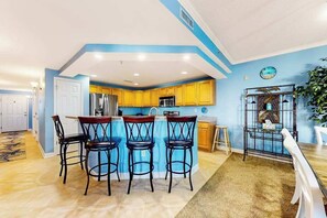 A kitchen with yellow cabinets, a blue island, and four black bar stools. - Bahia Vista II 304 (Ocean City)