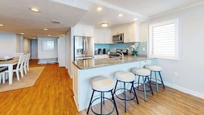 A modern kitchen with white cabinets, a stainless steel refrigerator, a microwave, and a bar area with stools. - Fountainhead Towers 1310 (Ocean City)