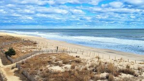 Une plage avec une clôture en bois, des dunes de sable et l’océan.