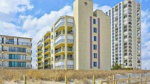 Un hôtel situé en bord de mer, composé de bâtiments à plusieurs étages, doté de balcons et donnant sur une plage de sable.