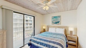 Ein Schlafzimmer mit einem Bett, einem Nachttisch, einem Deckenventilator, einem Gemälde und einer Glastür zu einem Balkon.