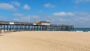 Un muelle se adentra en el océano, con un edificio al final, una playa de arena y un cielo despejado.