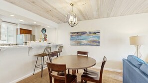 Un comedor con una mesa redonda y sillas, una cocina con refrigerador y armarios, y un cuadro en la pared.