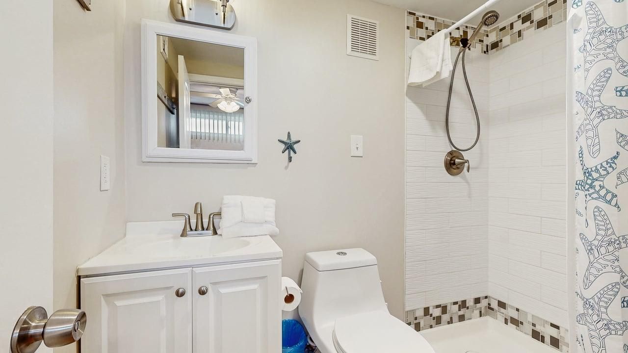 A bathroom with a toilet, sink, mirror, shower, and decorative starfish.