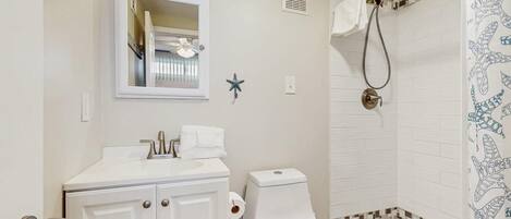 A bathroom with a toilet, sink, mirror, shower, and decorative starfish.