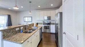 Cozinha moderna com bancadas de granito, eletrodomésticos de aço inoxidável e armários brancos.
