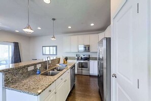 Cocina moderna con encimeras de granito, electrodomésticos de acero inoxidable y armarios blancos.