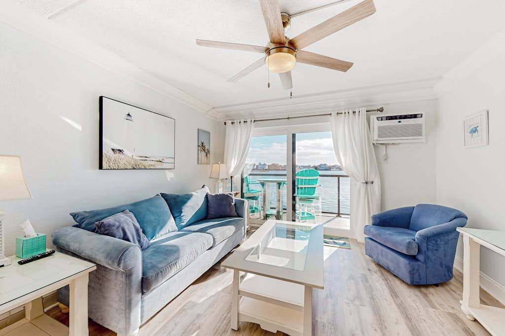 A modern living room with a sofa, a coffee table, a chair, a ceiling fan, and a view of the sea.