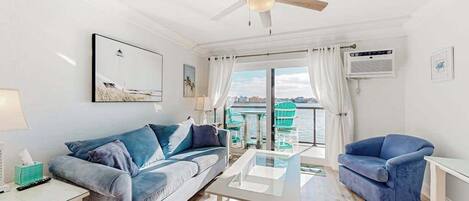 A modern living room with a sofa, a coffee table, a chair, a ceiling fan, and a view of the sea.