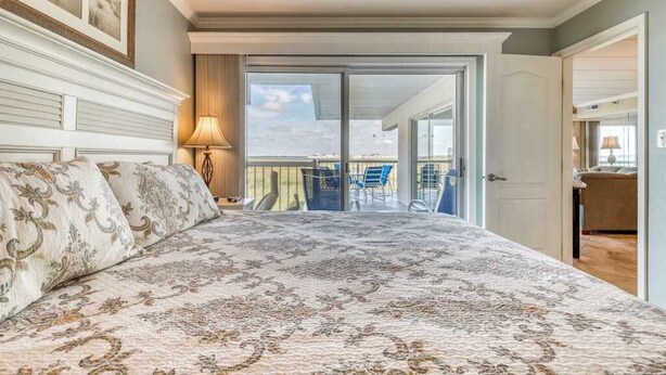 A bedroom with a large bed, a balcony with chairs, and a view of the sky. - Triton's Trumpet B 101 (Ocean City)