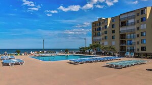 Ein Poolbereich mit Liegestühlen, ein Gebäude mit mehreren Balkonen und Blick aufs Meer.