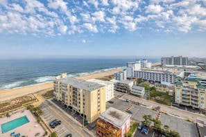 A coastal hotel with multiple buildings, a parking lot, and a beach view. - Oceanview condo with private balcony, shared pool access - walk to the beach (Ocean City)