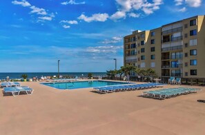A pool area with lounge chairs, a building with multiple balconies, and a view of the ocean. - Condo with beautiful ocean and bay views, central AC, and pool access (Ocean City)