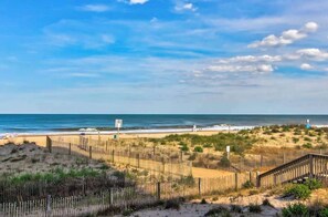A beach with a wooden fence, a lifeguard tower, and a sandy area with sparse vegetation. - Condo with beautiful ocean and bay views, central AC, and pool access (Ocean City)