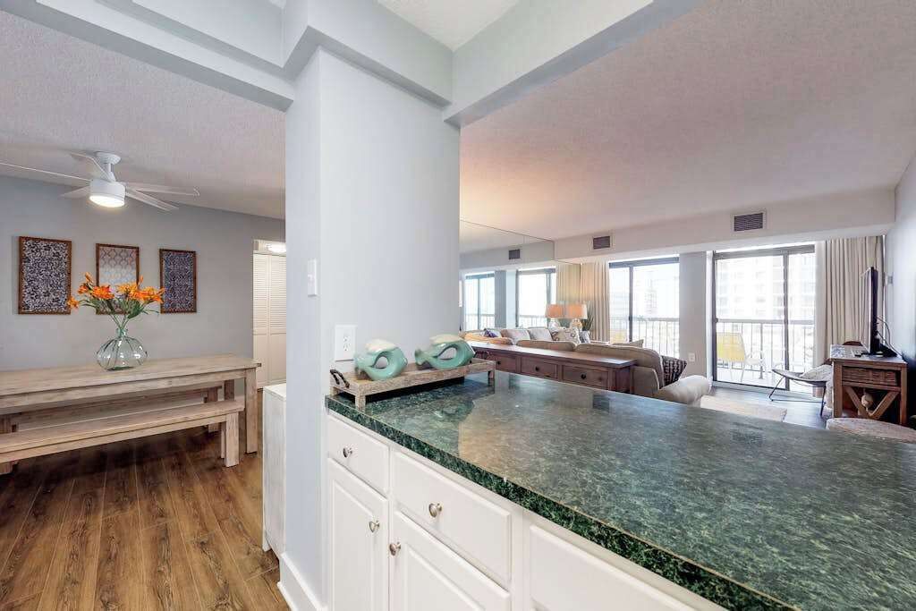 A spacious kitchen with a large island, wooden flooring, and a view to the living area.