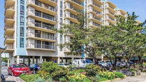 Un hotel de varios pisos con balcones, zona de estacionamiento y jardín ajardinado.