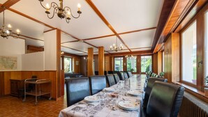 Una larga mesa de comedor lista para una comida, paredes de madera y ventanas grandes.