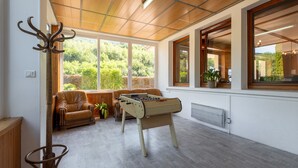 Una habitación con mesa de fútbol de mesa, sofá de cuero y ventanas amplias con vistas a la vegetación.