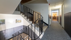 A staircase with a black railing, a carpeted floor, and a hallway leading to a room with a door. - Gite Les Sources (30 people) - Hautes Vosges (Bussang)