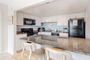 Eine Küche mit weißen Schränken, einer Granit-Arbeitsfläche, einem schwarzen Kühlschrank und einer Mikrowelle.