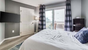 Ein Schlafzimmer mit Bett, Wandfernseher, Tür und Blick ins Freie.