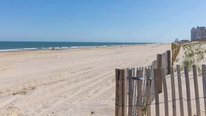 Ein Strand mit Holzzaun, Meer und Gebäuden im Hintergrund.