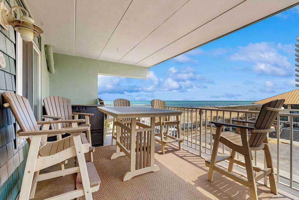 A balcony with wooden chairs and a table, overlooking a beach.