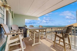 Un balcón con sillas y mesa de madera, con vista a la playa.