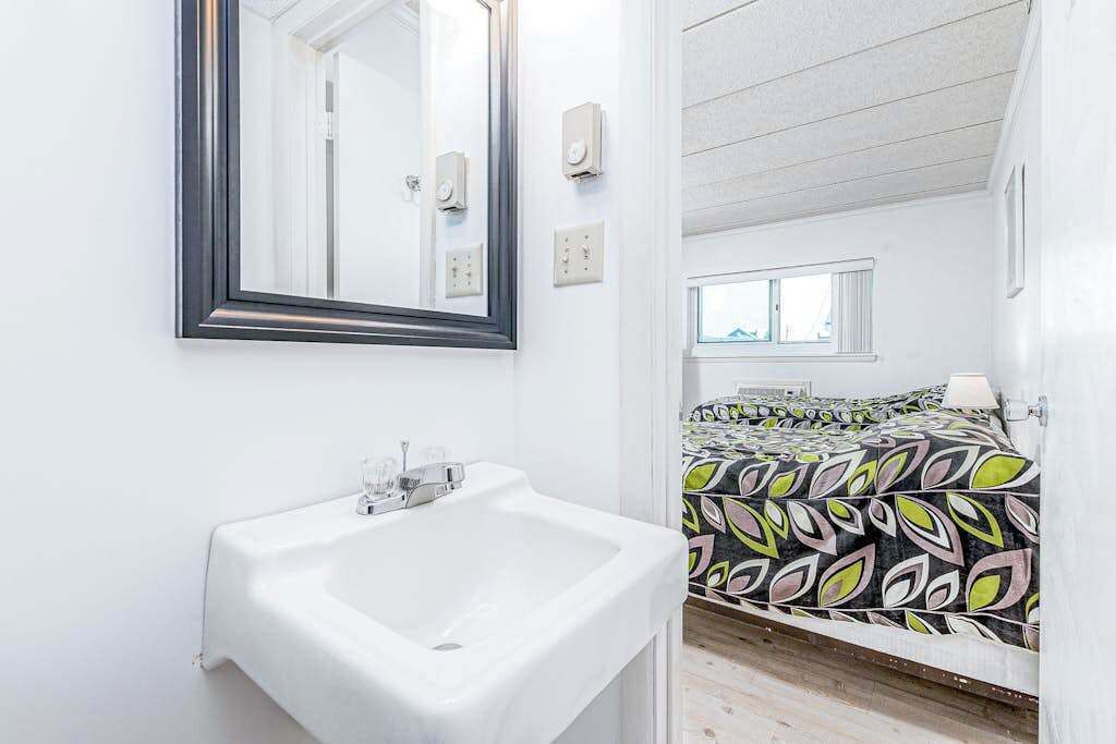 Een badkamer met een wit wastafelmeubel, een spiegel en een bed met een kleurrijk beddegoed.