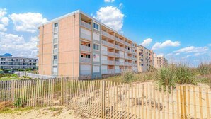 A multi-story hotel with balconies, located near a beach with a wooden fence. - Barefoot Country 303 (Ocean City)
