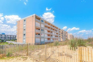 Ein mehrstöckiges Hotel mit Balkonen in der Nähe eines Strandes, der von einem Holzzaun begrenzt wird.