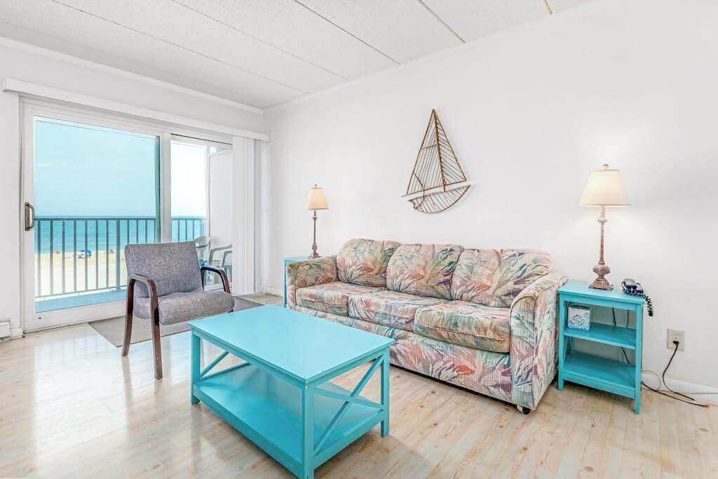 A room with a sofa, a chair, a table, a lamp, and a wall decoration.